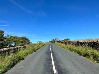 The Clitheroe to Skipton road, with dry stone walls, wild plants and trees, set against a blue sky near Slaidburn, UK