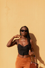 Portrait of a black woman, young, with braids in her hair, wearing sunglasses, on a plain yellowish colored background