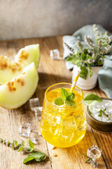 Fresh refreshing fruity summer drink, seasonal beverages. Melon lemonade in glasses with ice and mint on a wooden rustic table.