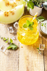 Fresh refreshing fruity summer drink, seasonal beverages. Melon lemonade in glasses with ice and mint on a wooden rustic table. Copy space.