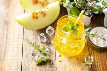 Melon lemonade in glasses with ice and mint on a wooden rustic table. Fresh refreshing fruity...