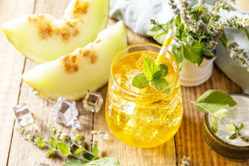 Fresh refreshing fruity summer drink, seasonal beverages. Melon lemonade in glasses with ice and mint on a wooden rustic table.