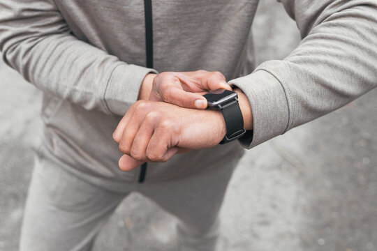 Unrecognizable man in sportswear standing and checking smart watch for time in daytime