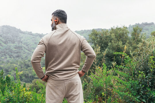 Unrecognizable man in sportwear standing in daylight against green trees and mountain