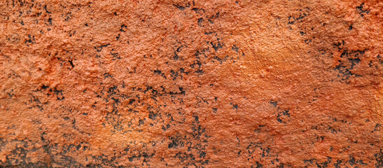 The texture of the rough cement wall with orange paint, the background of the rough cement wall with orange paint, taken from a close-up angle