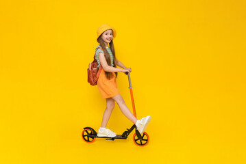A teenage girl rides a scooter in shorts, a panama hat and with a backpack. Summer sports and...