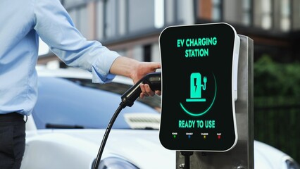 Businessman recharge his electric car from charging station at city center or public car park. Eco...