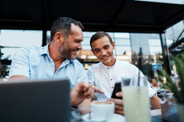 Handsome and happy father and his teenager son sitting in a restaurant and talking.