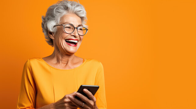 An elderly woman smiling and laughing with her phone against an orange background.
