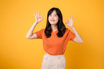 Embrace positive vibes as a young Asian woman in her 30s, donning an orange shirt, showcases the okay sign gesture on a sunny yellow background. Hands gesture concept