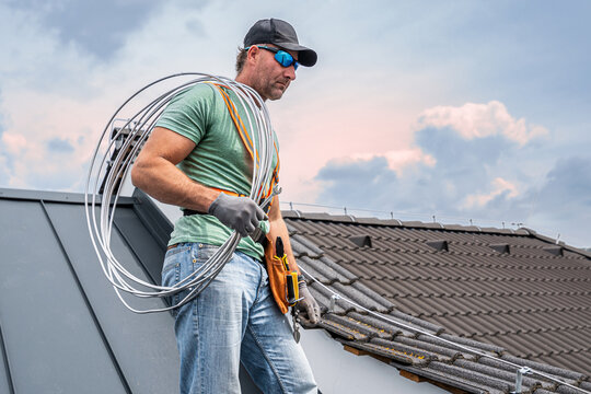 Work on the roof. An electrician installing a lightning rod conductor on a tiles roof.