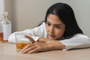 Obraz na płótnie Canvas Alcoholism drunk asian young woman hand holding glass of alcohol or whiskey, female sitting alone, drinking on table at home, at night. Treatment of alcohol addiction, suffer abuse problem alcoholism