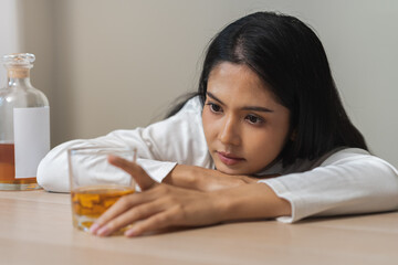 Alcoholism drunk asian young woman hand holding glass of alcohol or whiskey, female sitting alone, drinking on table at home, at night. Treatment of alcohol addiction, suffer abuse problem alcoholism