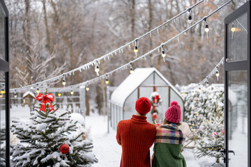 Young couple spend winter time together, standing back near Christmas tree and enjoy beautiful snowy weather at backyard