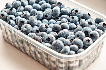 Fresh blueberries from the forest in a plastic container on a white background. Side view