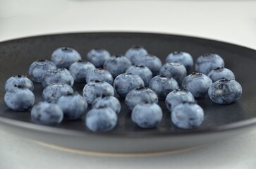 A bunch of blueberries on a black textured plate on a white background, close up