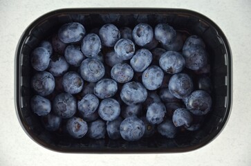 Blueberries in a black plastic container on a white background, top view
