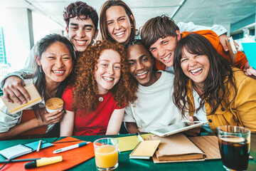 Multiracial university students sitting together at table with books and laptop - Happy young...