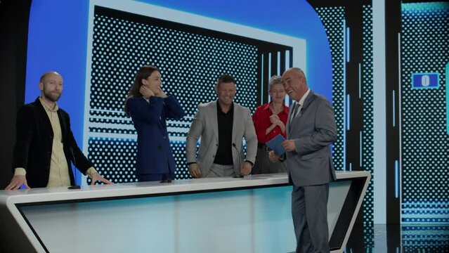 Funny charismatic host talking to the contestants during recording of a fictional morning family game show