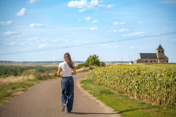 Jeune femme qui marche sur une route de campagne à coté d'une église