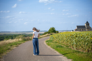 jeune femme sur une petite route de campagne au bord d'un champs de tournesol