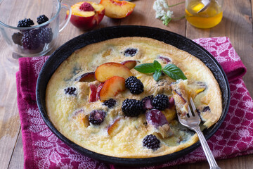 Omelette with peaches and blackberry in pan on wooden table