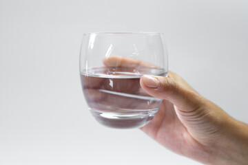 A glass of water held in a hand on a white background, hydration of the body on hot days