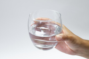 A glass of water held in a hand on a white background, hydration of the body on hot days