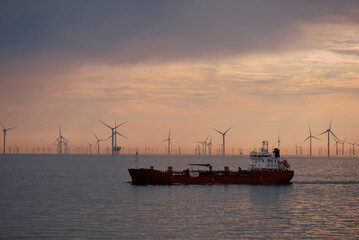 Fototapeta premium Handy-size tanker underway during calm weather in the North Sea with a park of wind generators in the background. Offshore sustainable energy generation. Offshore wind generation technology