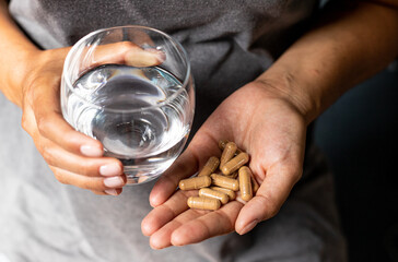 Consuming dietary supplements, ashwagandha capsules held in hand with a glass of water