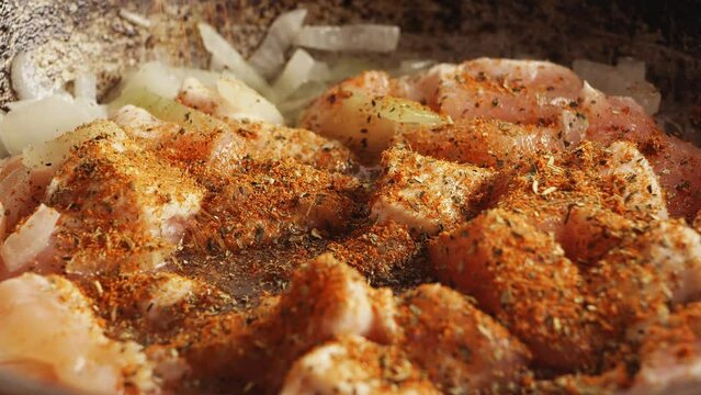 Pieces of chicken fried in a cast-iron skillet in oil with onions sprinkled with spices