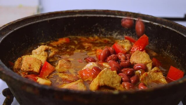 Chicken in spices with sumac for cholent, red beans are poured into a frying pan