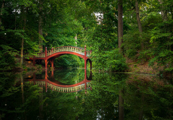 Ornate wooden bridge over very calm Crim Dell pond on campus of William and Mary college in...