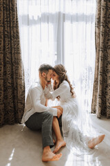 Beautiful, sexy bride in a white robe, groom in a white shirt hugs the bride against the background...