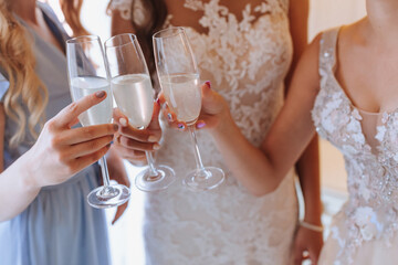 Young bridesmaids drink champagne in the bride's room. Beautiful women celebrating bachelorette party standing in room and with champagne. close-up photo of hands in glasses