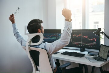 Yes Back view of stock trader with raised hands looking at multiple computer screens with data and charts and feeling happy while sitting in modern office
