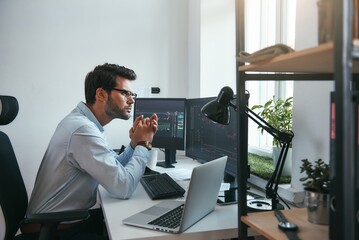 Concentrated on work. Side view of smart young male stock market broker analyzing a graphs on computer while sitting in his modern office