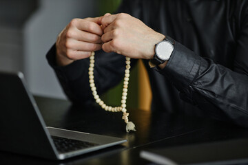 Closeup of unrecognizable man holding rosary while praying at desk in office, copy space