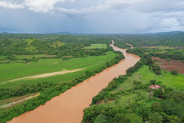 AERIAL: Big brown river flows among soaked meadows and fields after heavy rains