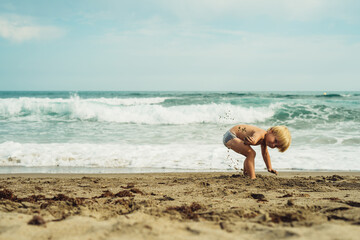 a little blond boy 3 years old is played in the sand on the seashore