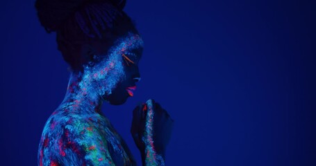 young African American woman looking down and praying Slow motion Body art glowing in ultraviolet light girl asks for blessing. copy space side view