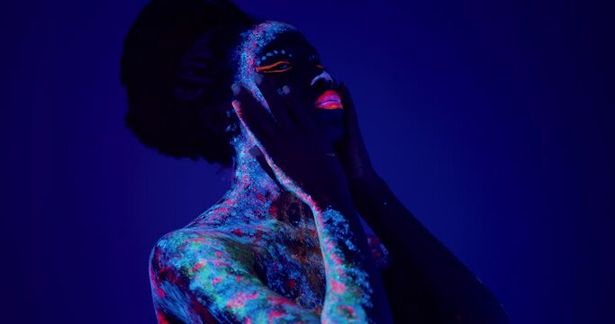 young woman enjoying UV pattern on her face, on the eyes and lips bright multi colored makeup. Graceful model posing with UV pattern on body. Slowmotion Girl touching face, cheecks, lips