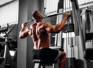 Fototapeta na wymiar Athlete muscular bodybuilder training back on simulator in the gym