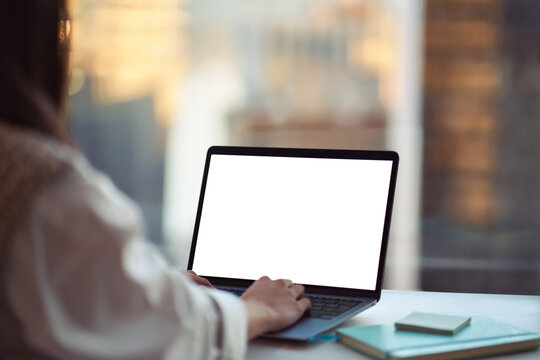 Business woman using laptop in office sitting at desk. Female hands typing on computer white blank mock up empty screen display for business websites or webinars ads. Over shoulder view. Close up