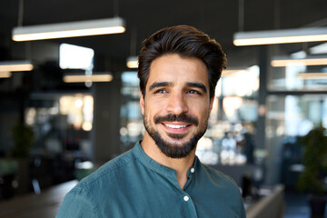 Smiling young business man looking away in office, headshot close up portrait. Happy Latin businessman, male entrepreneur, professional manager or company employee worker standing at work.