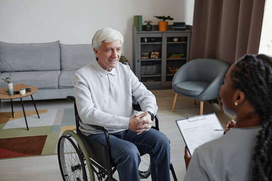 Portrait of white haired senior man with disability talking to nurse in retirement home, copy space
