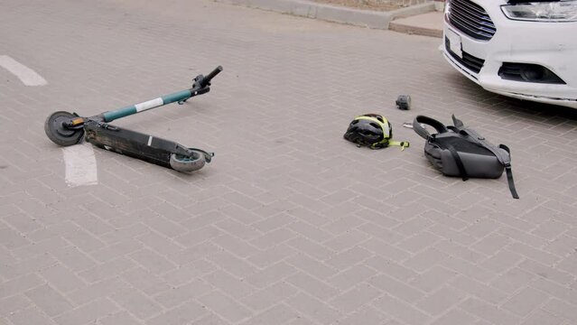 Detailed images of a road accident between a white luxury car and an electric scooter on a paved road.The cyclist's helmet, rucksack and pieces of the car are thrown on the ground.Concept of accidents