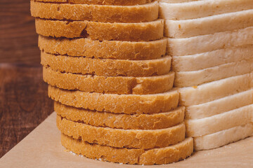 Sliced white bread with brown crust closeup on parchment paper on the wooden table.