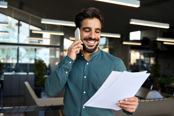 Smiling happy young bearded Latin professional business man executive holding documents and cell...