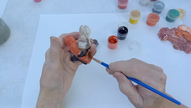 old woman painting plaster product, sitting at table. Closeup of old lady hand. Drawing in old age, development of cognitive abilities, prevention of senile diseases. art therapy